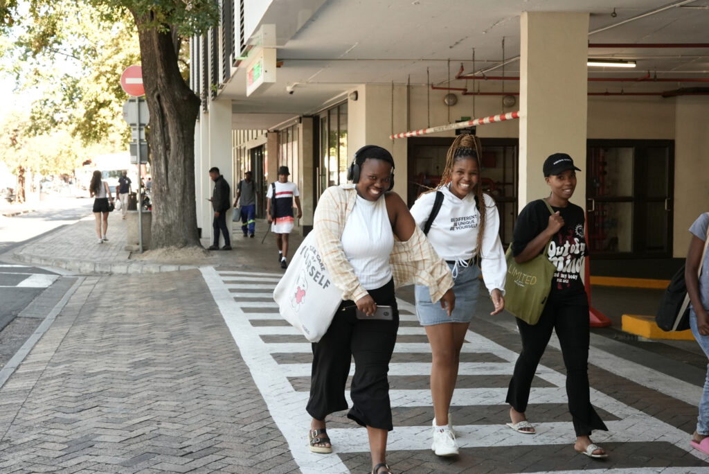 Three students smiling as they cross a street.