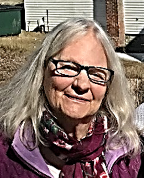 A woman wearing a scarf and glasses smiling outdoors.