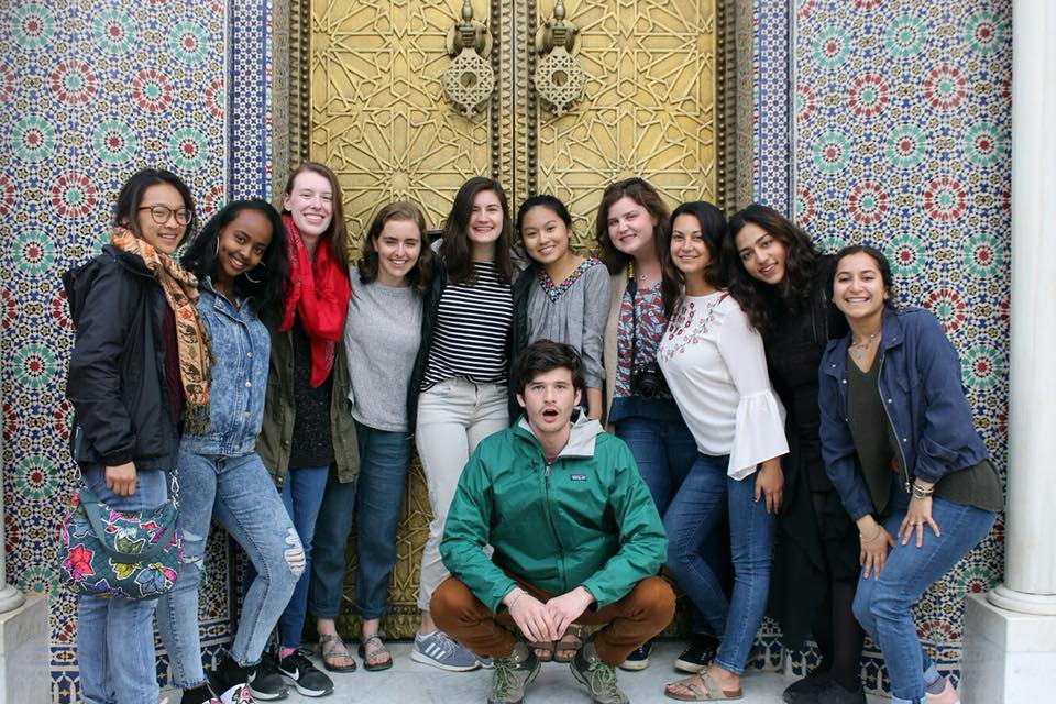 Eleven students posing in front of an ornate gold door and walls with mosaic tiles.