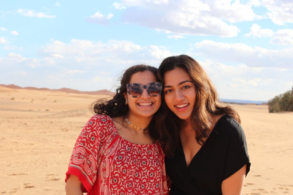 Two women smiling with arms around each other, standing in a desert.
