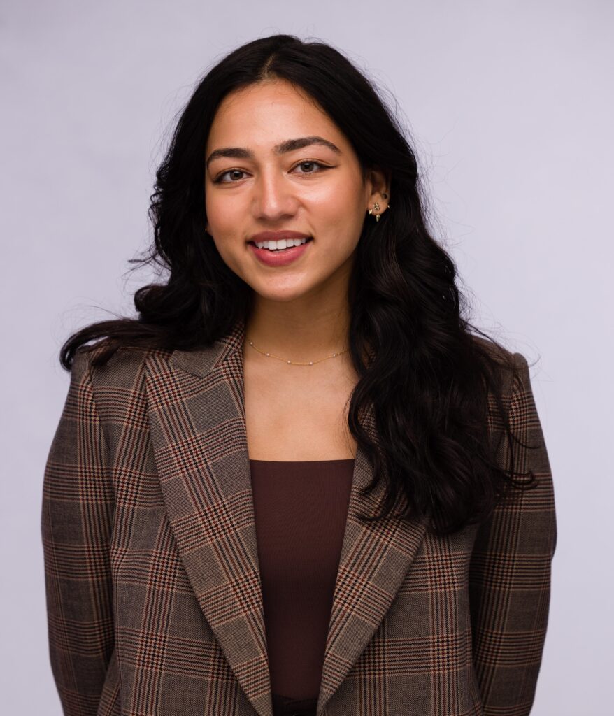 Headshot of a woman with long black hair wearing a plaid suit jacket.