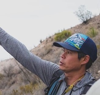 A man in a hat points to the sky in an outdoor setting.