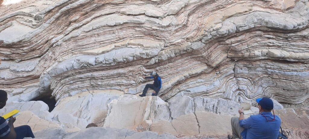An adult explores a large multilayered rock formation while two others watch.