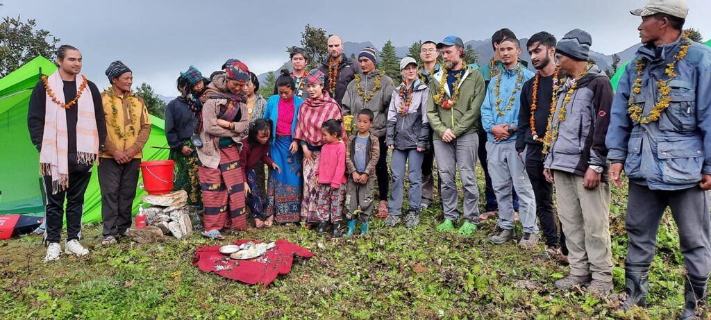 A multicultural group of people stand together in an outdoor setting; some are wearing wreaths around their necks.