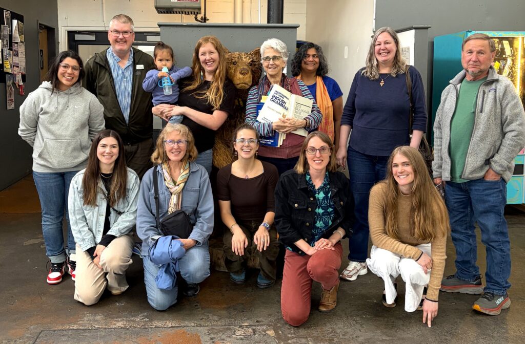 Thirteen SIT alumni pose for a photo in two rows in the lobby of a restaurant.